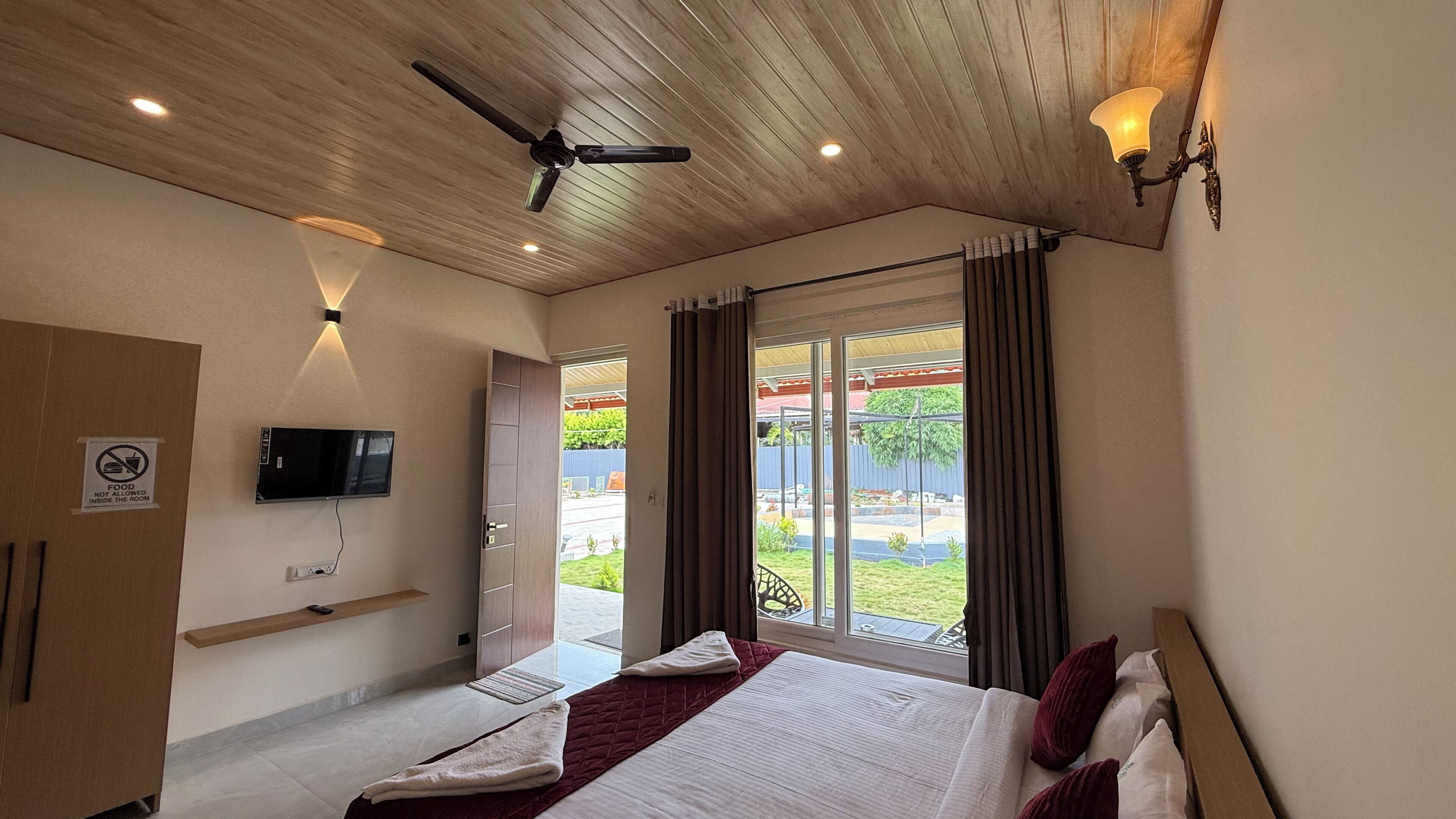 Habitación de hotel con cama, televisor, ventilador de techo y vistas al exterior.