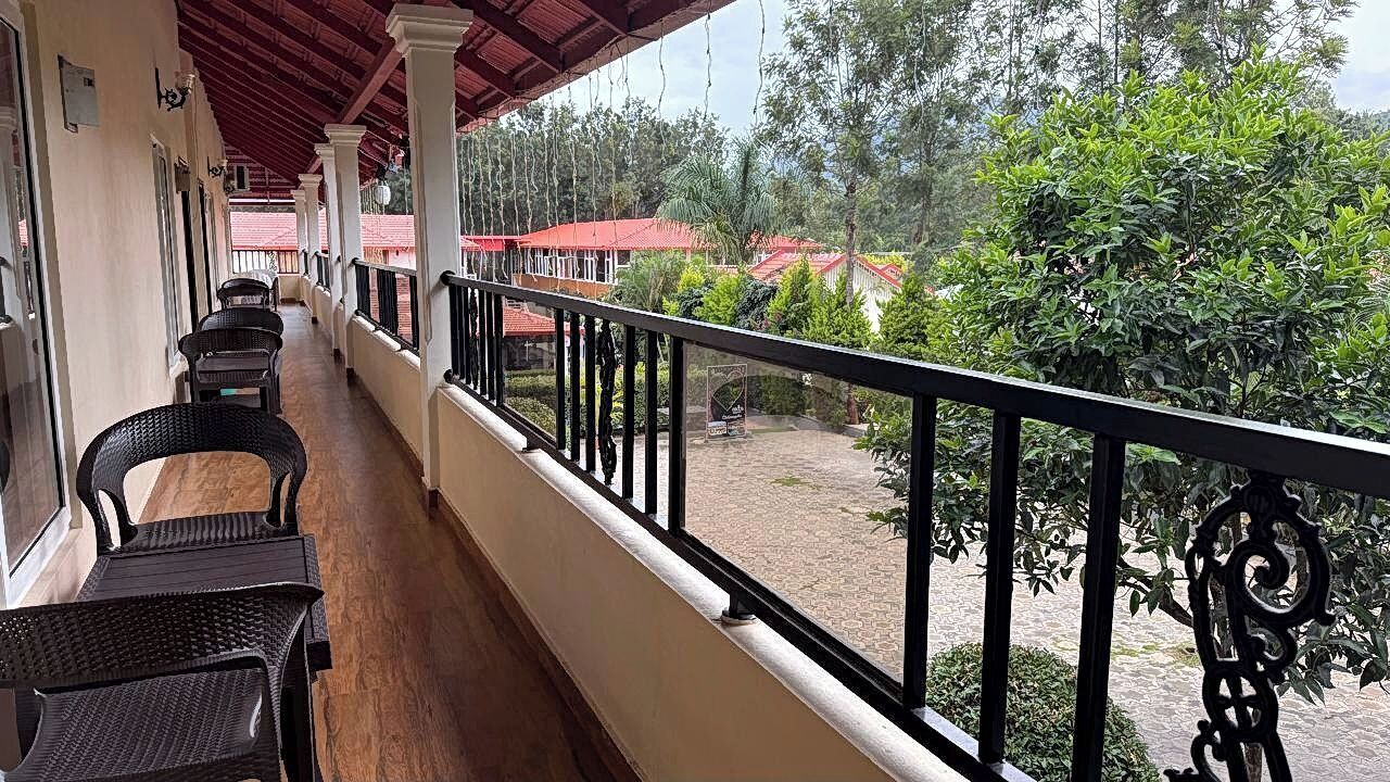 Un balcón techado con muebles de mimbre negro, una pared blanca y vistas a edificios con tejados rojos.