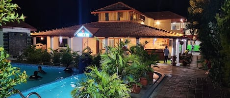 Un complejo turístico con piscina, un edificio bien iluminado y un camino pavimentado.