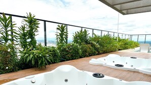 Una terraza en la azotea con cubierta de madera, dos tinas de hidromasaje blancas y abundante vegetación.