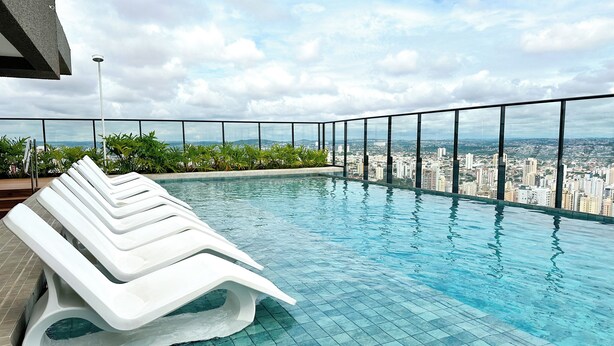 Una piscina infinita con sillas de descanso blancas, rodeada de vistas a la ciudad.