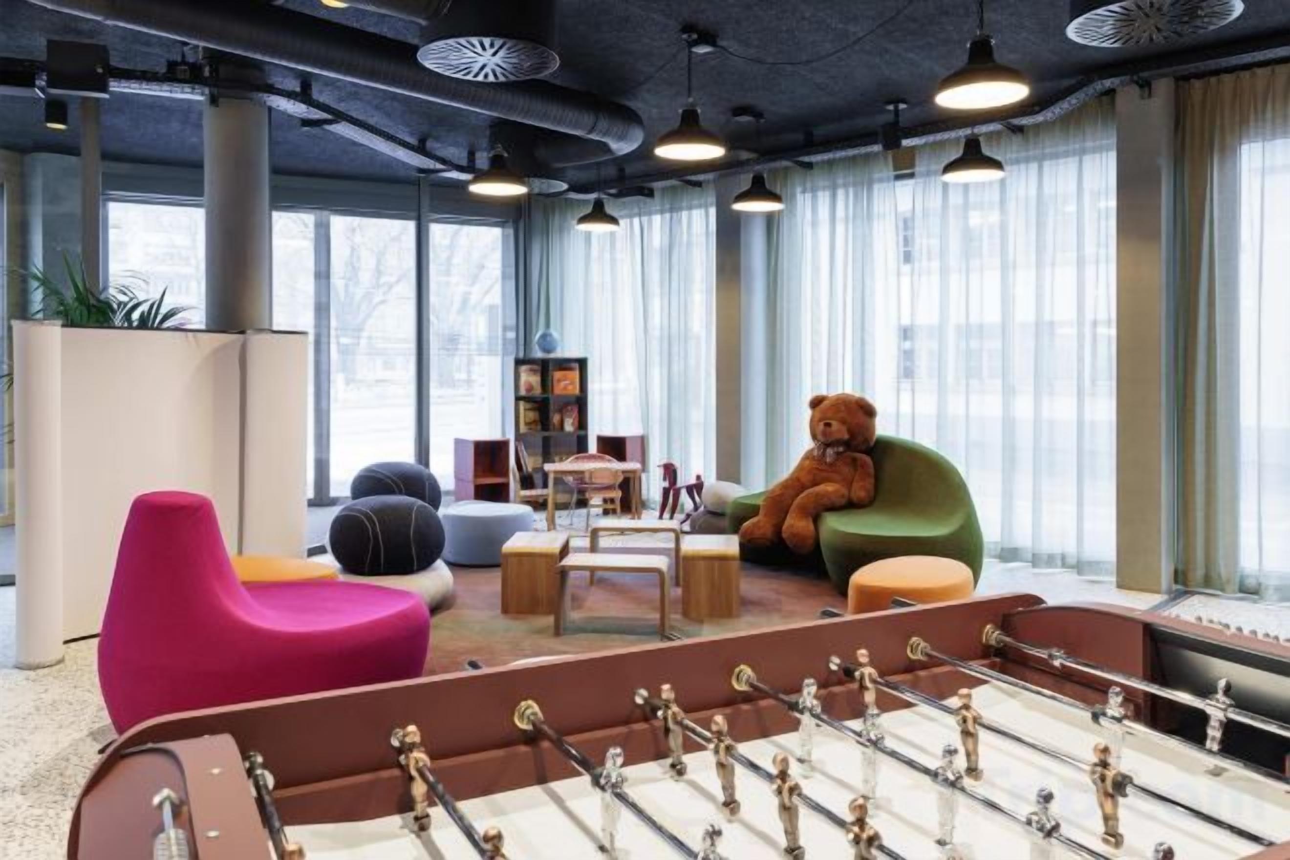 Un área de descanso moderna con mesa de futbolín, asientos coloridos y ventanas amplias.