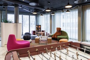 A modern lounge area with a foosball table, colorful seating, and large windows. - Ibis Styles Bern City (Berne)