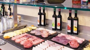 Assortimento di salumi e formaggi su un vassoio di vetro, con bottiglie di vino sullo sfondo.