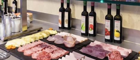 A variety of meats and cheeses on a glass counter with wine bottles behind.