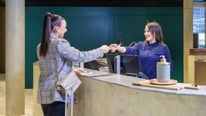 Una reception con un bancone, un gesto di stretta di mano tra due persone e una piccola bottiglia di disinfettante per le mani sul bancone.
