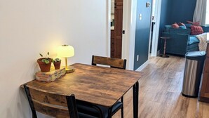 A dining area with a wooden table, two chairs, a lamp, and potted plants.