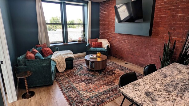 A modern living room with a brick wall, a flat-screen TV, a green sofa, a coffee table, and a dining table.