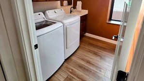 A laundry room with a washing machine and dryer, wooden cabinets, a sink, and a window with a view.