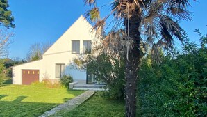 Et moderne hus i to etager med hvide facader, en brostenssti der fører til hoveddøren, og en palme i forgrunden.
