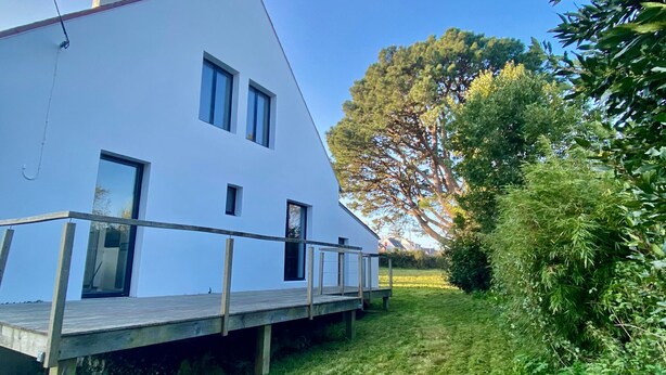 En moderne hvid bygning med en træterrasse og et stort træ i baggrunden.