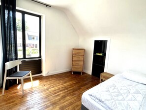 A bedroom with a wooden floor, a bed with a quilted white duvet, a wooden dresser, a chair, and a window with a view of the outside. - Charming house between Port Tudy and Le Bourg in Groix (Groix)