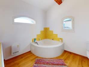 Un bagno con vasca da bagno angolare, pareti piastrellate di giallo, pavimento in legno e tappeto colorato.