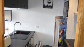 Una cocina compacta con pileta, lavavajillas y refrigerador repleto de diversos artículos.