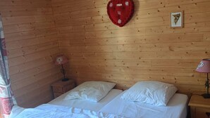 Een houten kamer met een bed, twee nachtkastjes, een decoratie in de vorm van een hart en een ingelijst foto aan de muur.