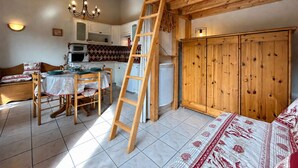 A loft-style room with a wooden ladder, a dining table with chairs, a kitchenette, and a large wardrobe. - Studio Cabin 5 pers, Parking, Near Slopes (Briançon)