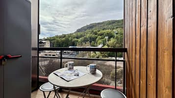 A balcony with a table and two chairs, overlooking a hilly landscape with a ski lift.