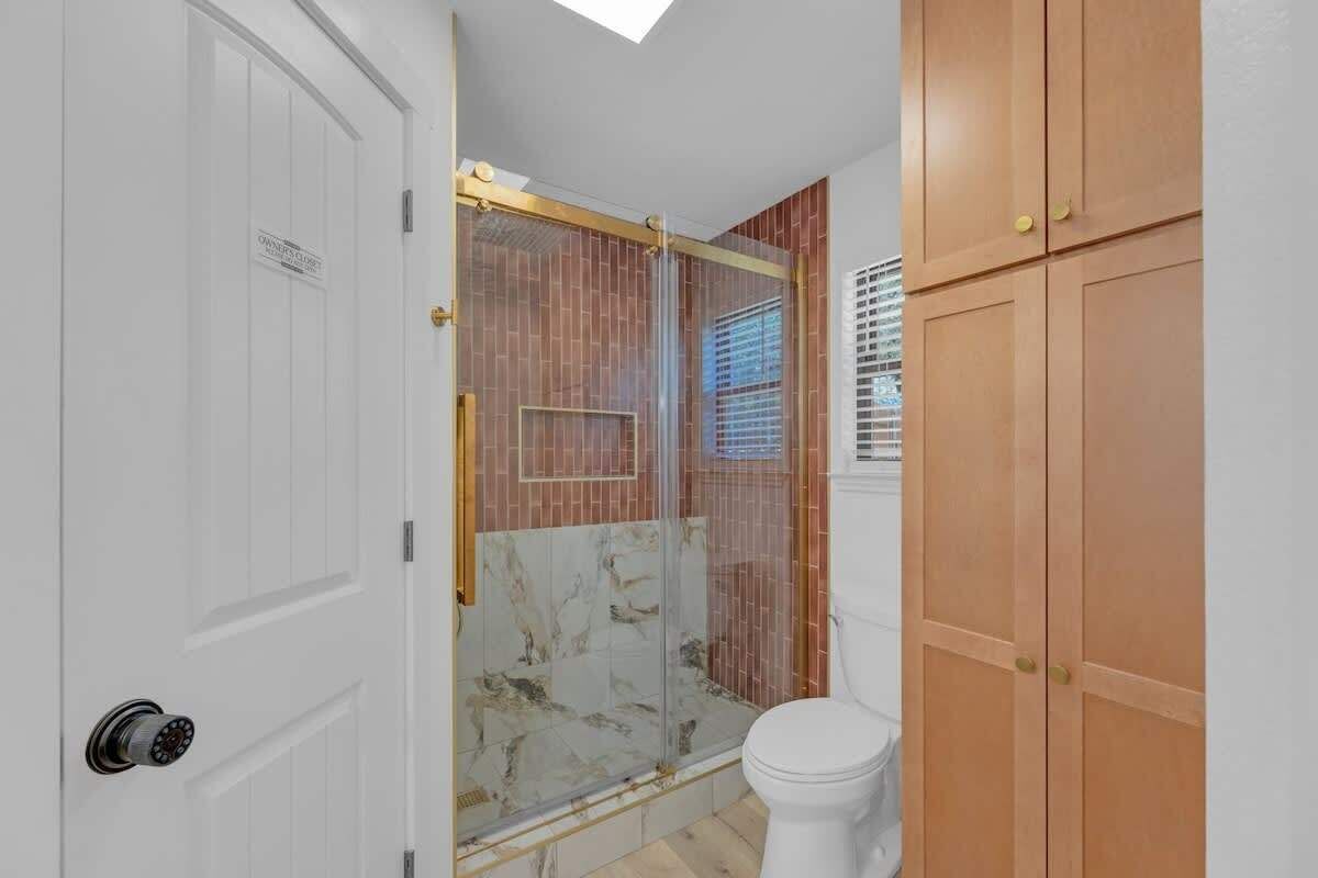 A bathroom with a shower, toilet, and wooden cabinets.