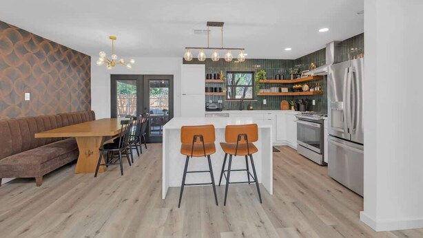 A modern kitchen with a central island, wooden dining table, and bar stools. - Hot Tub | Speakeasy | Basketball Court | Sleeps 12 (Cedar Park)