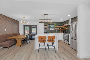 A modern kitchen with a central island, wooden dining table, and bar stools. - Hot Tub | Speakeasy | Basketball Court | Sleeps 12 (Cedar Park)