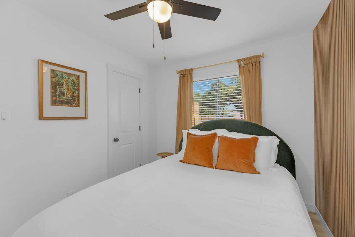A bedroom with a bed, a ceiling fan, a window with curtains, and a framed picture on the wall.