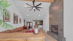 A modern living room with a fireplace, wooden ceiling beams, and a dining area with a wooden table. - Hot Tub | Speakeasy | Basketball Court | Sleeps 12 (Cedar Park)