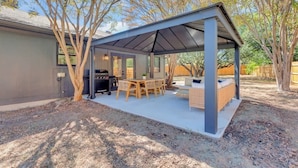 A covered patio area with a grill, wooden table, and seating. - Hot Tub | Speakeasy | Basketball Court | Sleeps 12 (Cedar Park)