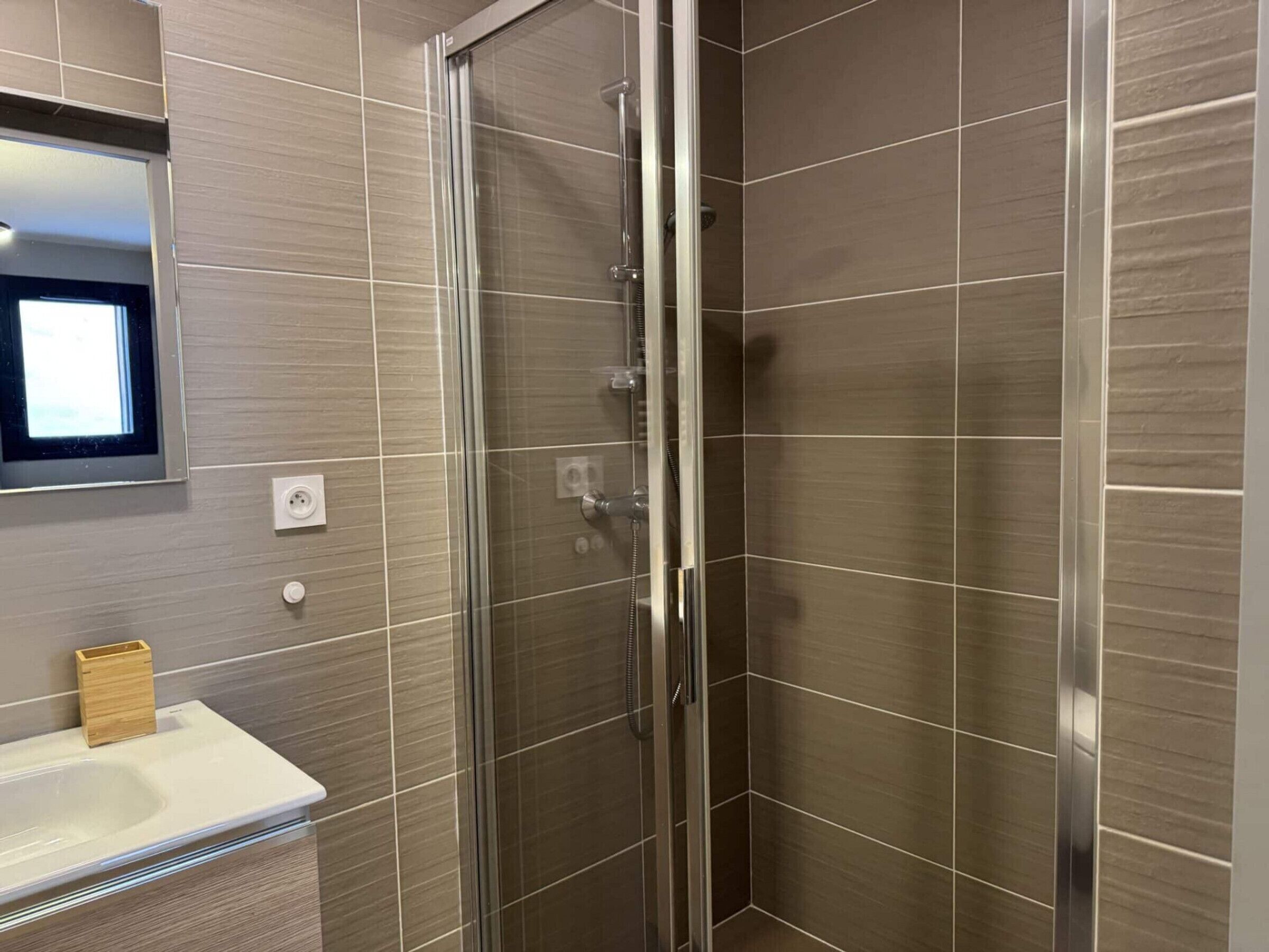 A modern bathroom with a glass-enclosed shower, a white sink, and a mirror above the sink.