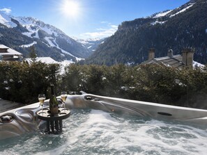 A hot tub with a mountain view, surrounded by snow-covered mountains and trees.