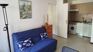 Ein gemütlicher Wohnbereich mit Sofa, Lampe, einem Gemälde und einer Küchenzeile.