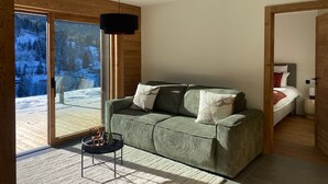 A modern living room with a green sofa, a small side table, and a large window offering a snowy mountain view.