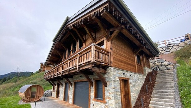 A wooden chalet with a balcony, stone walls, and a wooden deck.
