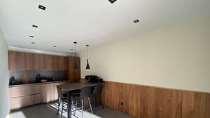 A modern kitchen with wooden cabinets, a dining area with a table and chairs, and recessed ceiling lights.