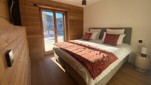 A bedroom with a large bed, wooden walls, and a sliding glass door to a balcony.