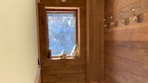 A wooden cabin with a window, a bench, and wall-mounted hooks.