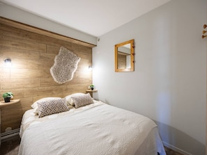 Ein Schlafzimmer mit einem Holzkopfteil, einem großen Spiegel und einem Bett mit gemusterten Kissen.