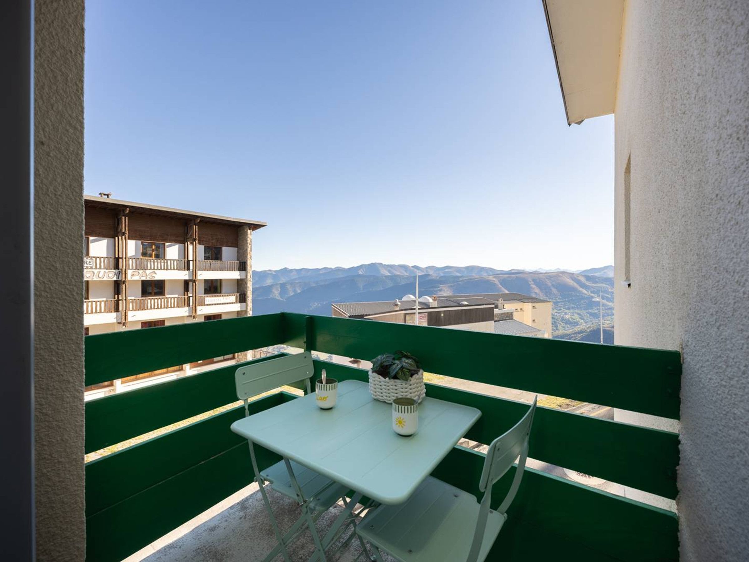 A balcony with a table and chairs, overlooking a mountainous landscape.