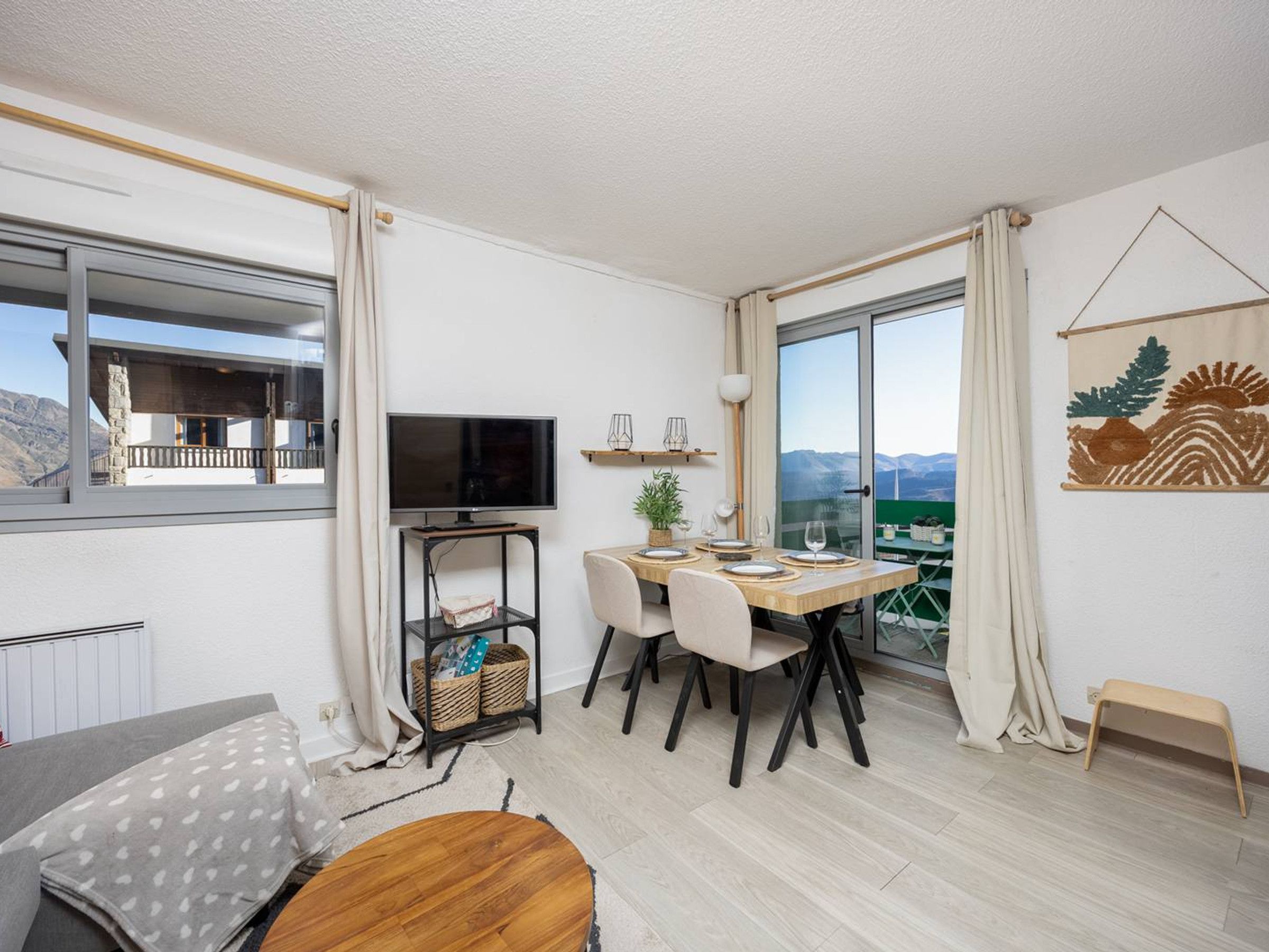 Ein modernes Wohnzimmer mit Essbereich, Fernseher und Blick auf die Berge.