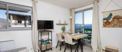 A modern living room with a dining area, a television, and a view of the mountains.