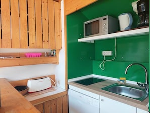 Una cocina compacta con armarios de madera, microondas, cafetera y lavavajillas Bosch.