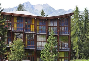 Un edificio de varios pisos con balcones, rodeado de árboles y montañas.
