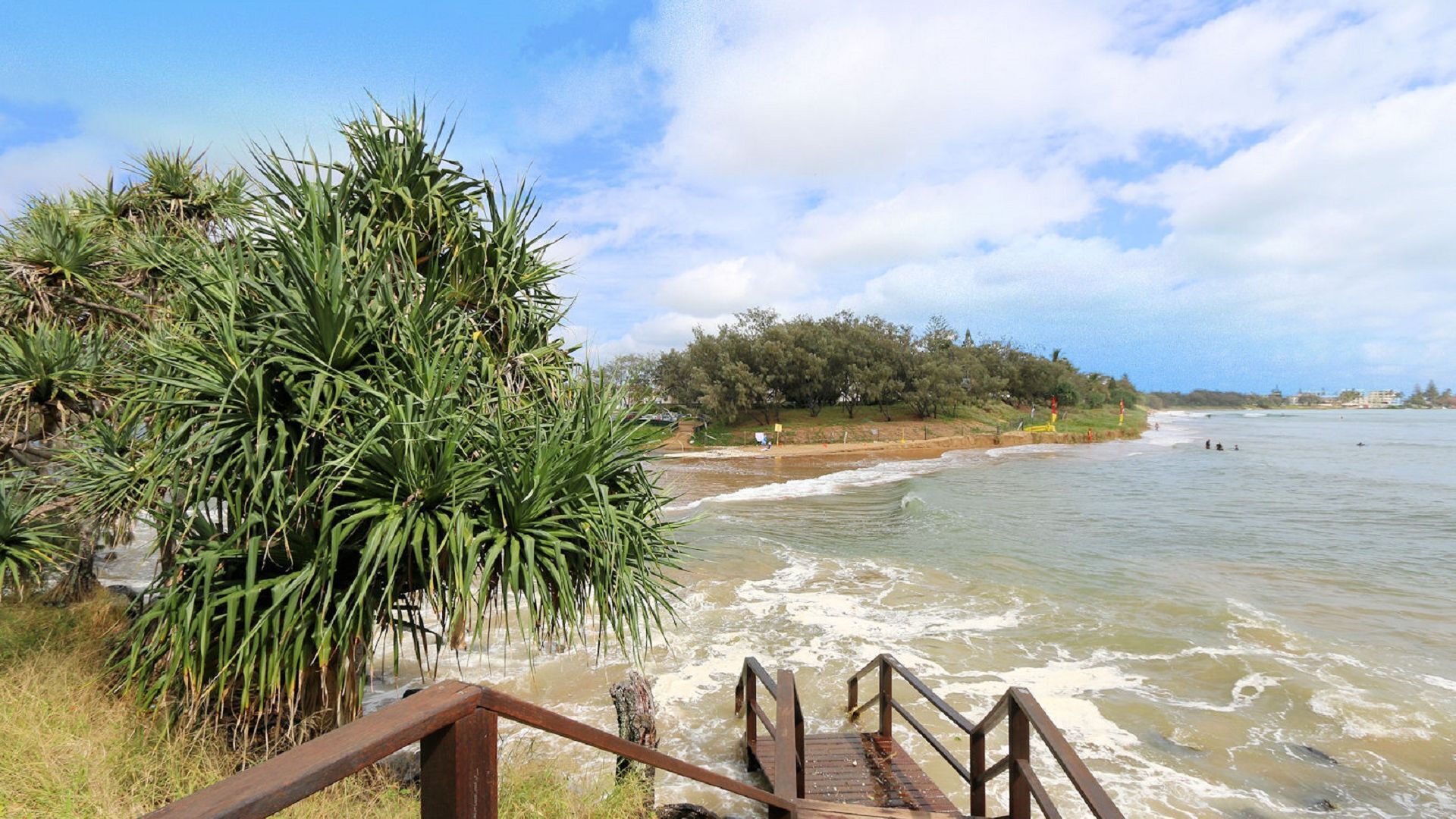 A wooden staircase leading to a beach with waves, surrounded by greenery and trees.