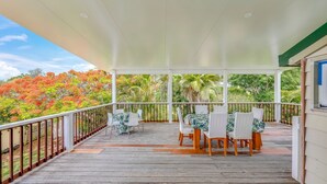 A covered outdoor patio with a wooden deck, white railings, and a table with chairs.