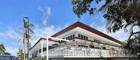En tvåvåningsbyggnad med ett takförsett utomhusområde med sittplatser, en skylt med texten ”Bargara Beach Hotel” och en palm som syns tydligt i förgrunden.