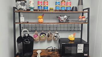 A kitchen with a coffee maker, a microwave, and shelves with bottles and kitchenware.