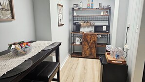 Une cuisine compacte avec une table en bois, une machine à café, un four à micro-ondes et un petit réfrigérateur.