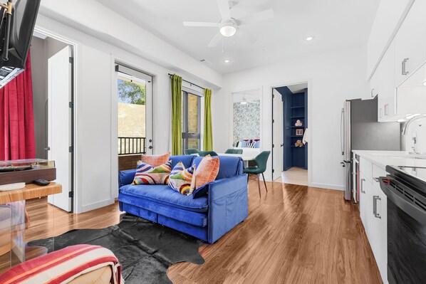 A modern living room with a blue sofa, a dining area, and a kitchen with white cabinets and a black stove. - Music Row Bungalow-Pool-Free parking-Rooftop-Near Gulch, Vanderbilt & Broadway (Nashville)