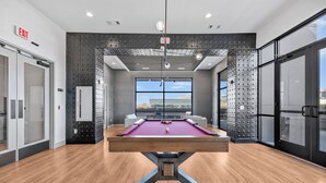 Une table de billard dans une pièce moderne, avec une grande fenêtre, un plafond orné d’un motif original et un panneau indiquant la sortie.
