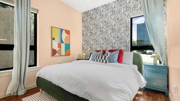 Une chambre à coucher avec un grand lit, une table de chevet, une commode et une fenêtre avec des rideaux.