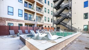 Un bâtiment moderne doté d’une piscine sur le toit, agrémentée de chaises longues blanches en forme de cygne et d’une bordure de piscine en briques.